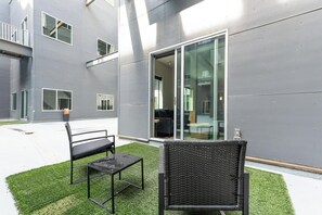 An outdoor seating area with two chairs and a table, a building with large windows, and a grassy surface. - Landing | Chic 2BD, Yoga Studio, Gym (Omaha)