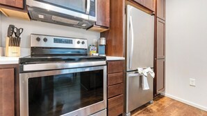 Eine Küche mit Edelstahl-Kühlschrank, Backofen und Mikrowelle. Holzschränke und eine Arbeitsplatte mit Messerblock ergänzen das Bild.