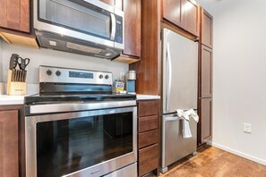 A kitchen with a stainless steel refrigerator, oven, and microwave. There are wooden cabinets and a countertop with a knife block. - Landing | Beautiful 2BD, Yoga Studio, Gym (Omaha)