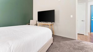 Ein Schlafzimmer mit einem Bett, einem Fernseher auf einem Schrank, einer Tür und einem Teppichboden.