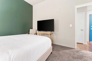 A bedroom with a bed, a television on a stand, a door, and a carpeted floor. - Landing | Beautiful 2BD, Yoga Studio, Gym (Omaha)