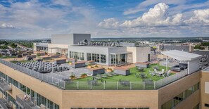 A rooftop terrace with outdoor seating, a modern building, and a clear sky. - Landing | Beautiful 2BD, Yoga Studio, Gym (Omaha)