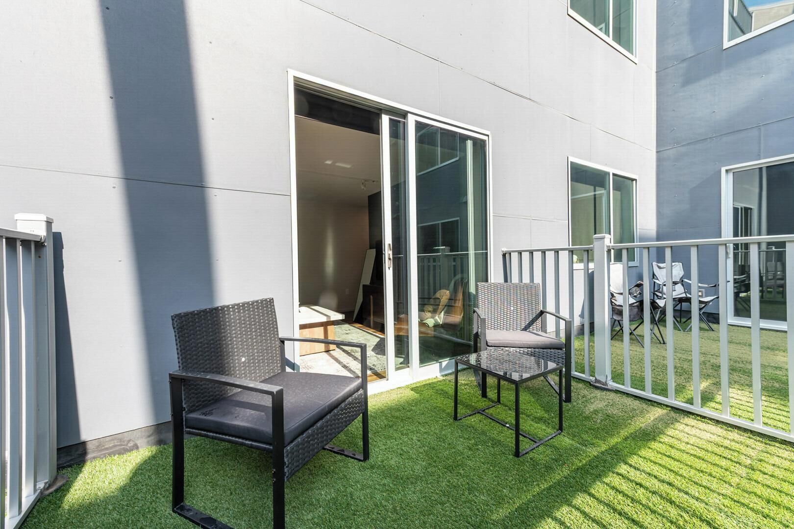 A balcony with two chairs and a table, a sliding glass door, and a view of the interior.