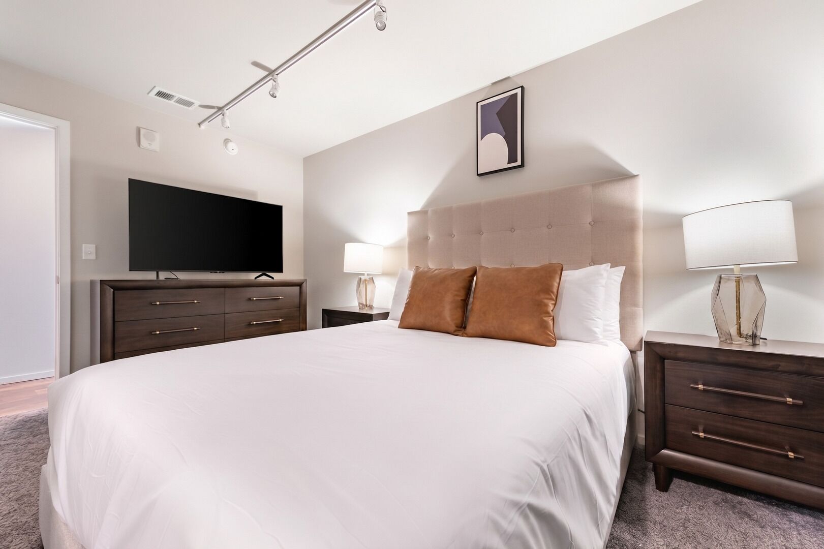 A hotel room with a large bed, a flat-screen TV, two bedside tables with lamps, and a wall-mounted artwork.
