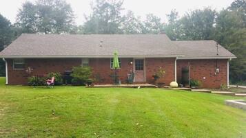 A two-story brick building with a front porch, a green umbrella, and a well-maintained lawn.