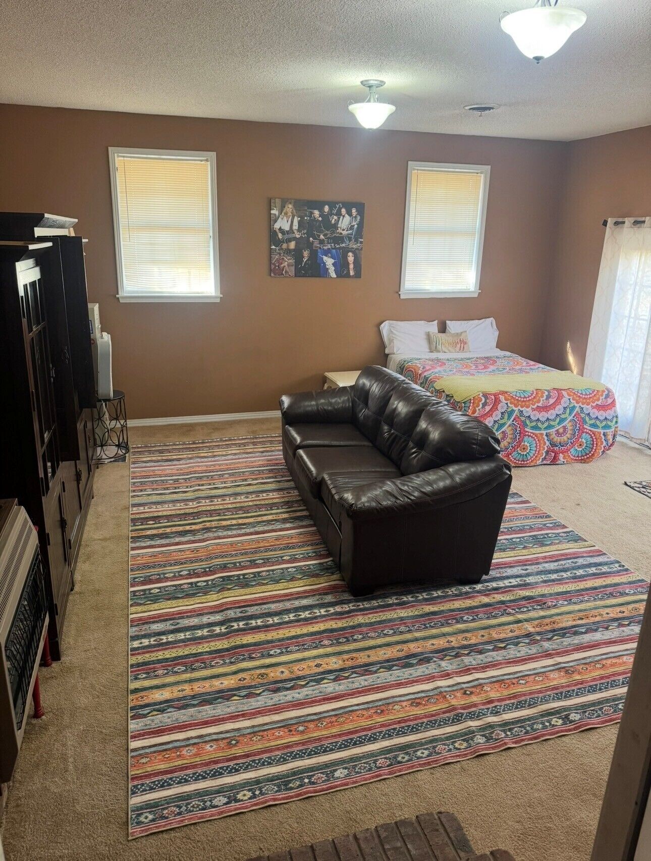 A bedroom with a bed, a sofa, a colorful rug, and a ceiling fan.