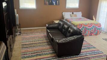 A bedroom with a bed, a sofa, a colorful rug, and a ceiling fan.