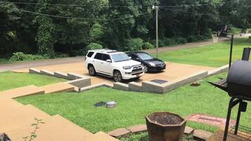 A backyard with a barbecue grill, a white SUV, and a black car parked on a paved area.