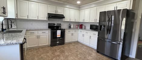 A kitchen with white cabinets, a stainless steel refrigerator, a stove, and a microwave.