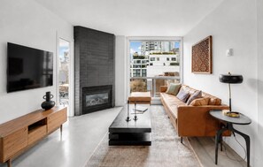 A modern living room with a flat-screen TV, a fireplace, a leather sofa, and a view of the cityscape. - Stylish Yaletown 2BR/2BA | Pool & Gym + Free Parking | Central Location (Vancouver)