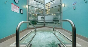 Un espace dédié aux bains à remous, doté d’une paroi en verre, de rampes en métal et d’un panneau indiquant les règles à respecter dans le spa.