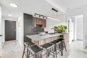 A modern kitchen with a central island, bar stools, and a wooden backsplash. - Stylish Yaletown 2BR/2BA | Pool & Gym + Free Parking | Central Location (Vancouver)