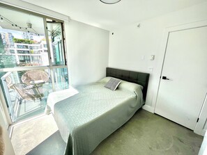 Ein Schlafzimmer mit Bett, Fenster und Blick auf Gebäude sowie einer Tür.