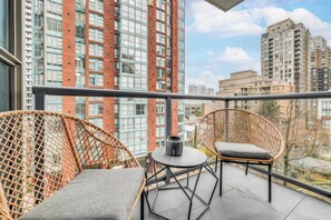 Ein Balkon mit Korbstühlen und einem kleinen Tisch, mit Blick auf eine Stadtlandschaft und hohe Gebäude.