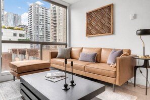 Un salon moderne avec un canapé en cuir, une table basse et une vue sur des immeubles de grande hauteur.