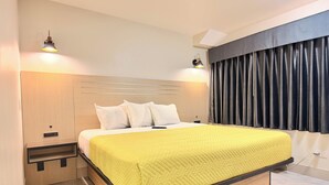 Habitación de hotel moderna con cabecera de madera, colcha amarilla acolchada, dos lámparas de noche y un ventanal con cortinas oscuras.
