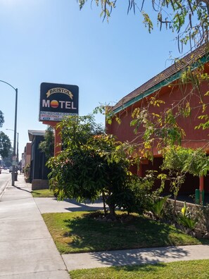 Un motel con un letrero grande, una acera y algo de vegetación.