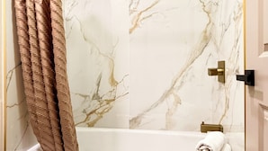 Un baño con ducha envuelta en vidrio, paredes de mármol, bañera y retrete.