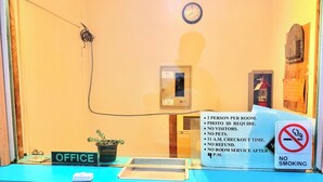 A reception desk with a sign indicating a 2 person per room policy, photo ID requirement, no visitors, no pets, 11 a.m. checkout time, no refund, and no room service after 4 p.m.