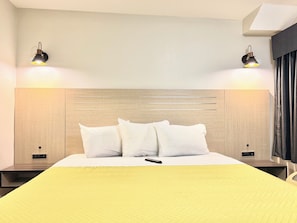 Quarto de hotel com cabeceira de madeira, duas mesas de cabeceira com luminárias, cama com roupa de cama branca e um edredom amarelo.