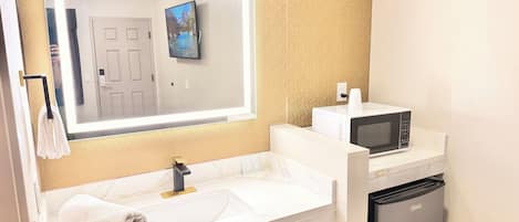 A bathroom with a sink, a mirror, a towel rack, a toilet, and a microwave.
