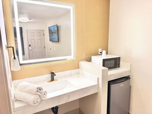 Un baño con lavamanos, espejo, toallero, inodoro y microondas.