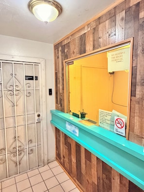 A reception area with a wooden wall, a blue counter, and a door with a metal gate. - BRISTOL MOTEL (Long Beach)