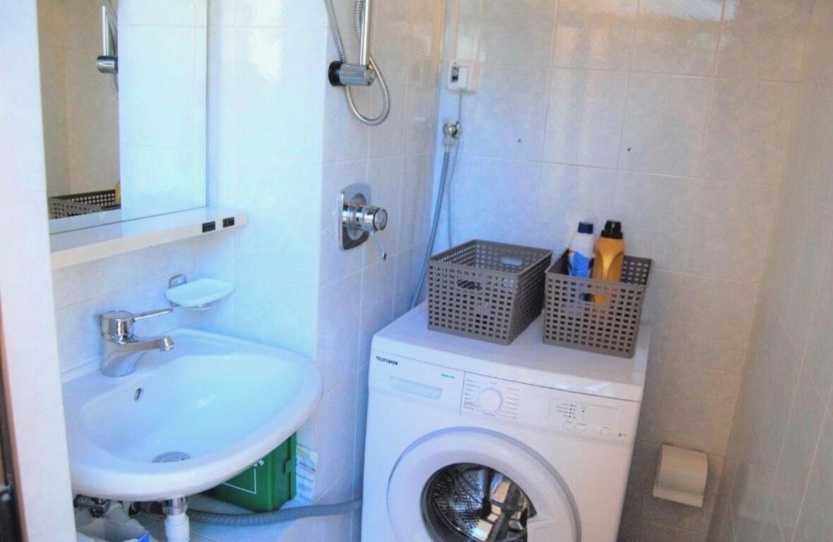 Une petite salle de bain comprenant un lavabo, un lave-linge et un miroir.