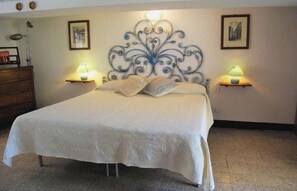 A neatly made bed with a white bedspread, two bedside lamps, and a decorative wall piece above the bed. - At Cà du Grillu (Albisola Superiore)