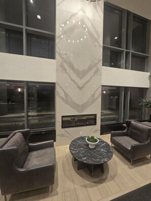 A modern interior with two leather sofas, a marble table with a bowl of decorative balls, and a wall-mounted fireplace. - Modern 1-Bedroom Condo with Full Amenities (Brampton)