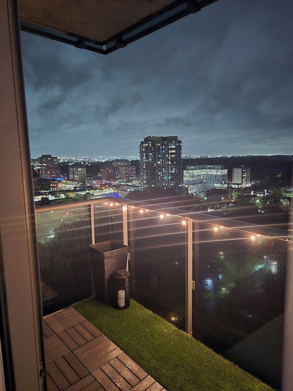 A view from a balcony with a cityscape in the background, a wooden deck, and string lights.