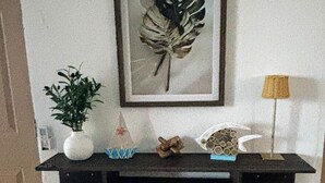 A wall-mounted shelf with a framed leaf artwork, a potted plant, decorative items, and a lamp. - 2-bedroom apartment in welcoming Mazatlán with AC for comfort (Mazatlán)