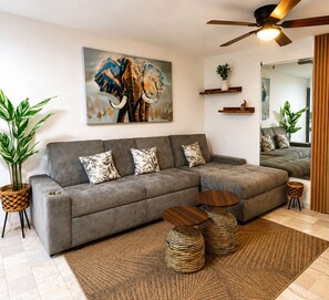 A modern living room with a grey sectional sofa, a large elephant painting, a ceiling fan, and a wooden floor. - 2-bedroom apartment in welcoming Mazatlán with AC for comfort (Mazatlán)