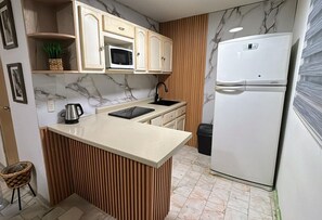 A compact kitchen with a microwave, a refrigerator, a sink, and a wooden island. - 2-bedroom apartment in welcoming Mazatlán with AC for comfort (Mazatlán)
