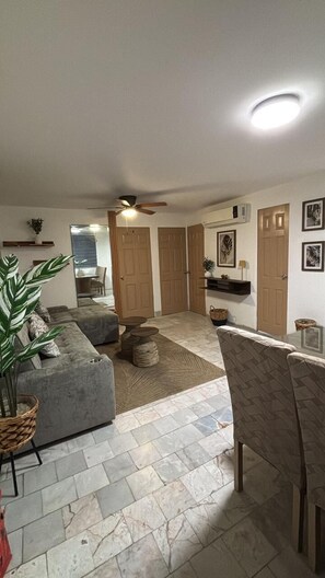 A spacious living area with a grey sofa, a dining table, and a ceiling fan. - 2-bedroom apartment in welcoming Mazatlán with AC for comfort (Mazatlán)