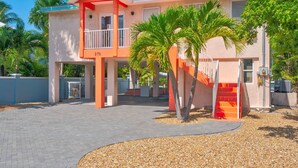 A two-story building with a red and white color scheme, a balcony, and a palm tree in the foreground. - Pet-Friendly Boater’s Retreat- Pool, Dock & Kayaks (Marathon)