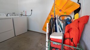A laundry room with a washing machine, dryer, and a metal rack with cleaning supplies. - Pet-Friendly Boater’s Retreat- Pool, Dock & Kayaks (Marathon)