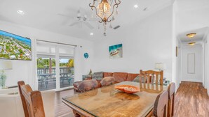A dining area with a wooden table, chairs, and a view of a balcony with outdoor furniture. - Pet-Friendly Boater’s Retreat- Pool, Dock & Kayaks (Marathon)