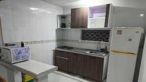 A kitchen with white tiled walls, a gas stove, a refrigerator, and wooden cabinets.
