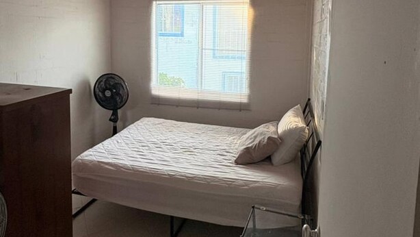 A bedroom with a bed, a desk, a chair, a window, and a wooden ceiling.