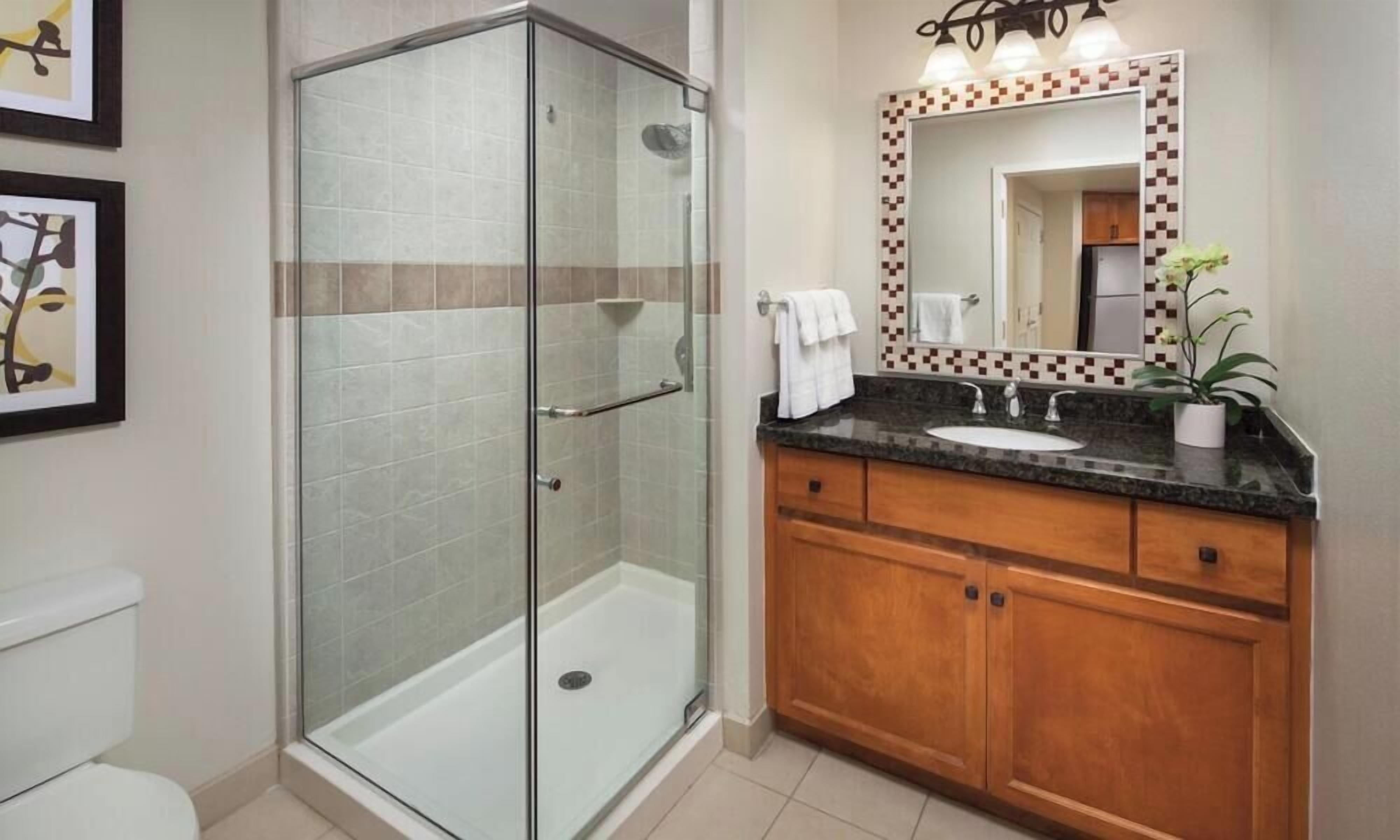 A bathroom with a glass-enclosed shower, a sink with a wooden vanity, and a mirror with a decorative frame.