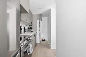 A modern kitchen with stainless steel appliances, a built-in oven, and a countertop with a kettle. - Roncesvalles Charm Stylish 1BR Near High Park! | Parking Available (Toronto)