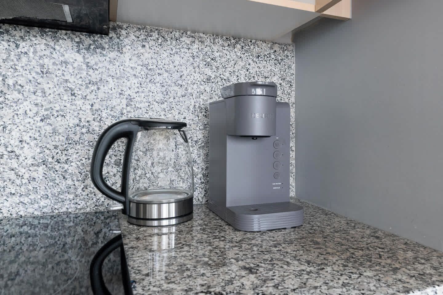 Une cuisine dotée d’un plan de travail en granit, d’une bouilloire en acier inoxydable et d’une machine à café grise.