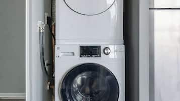 Un appareil compact combinant lave-linge et sèche-linge, installé dans une petite buanderie avec un plancher en bois et un mur blanc.