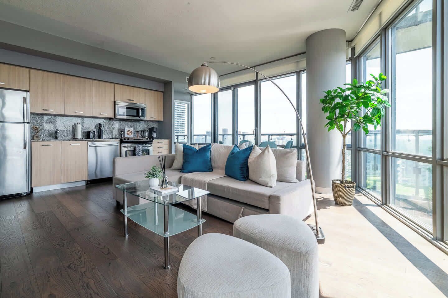 Een moderne woonkamer met een glazen salontafel, een bank met blauw-witte kussens en een groot raam met uitzicht op de stad.