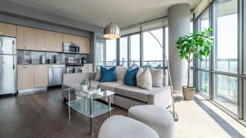 Un salon moderne avec une table basse en verre, un canapé agrémenté de coussins bleus et blancs, et une grande fenêtre donnant sur la ville.