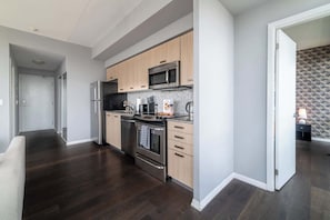 A modern kitchen with stainless steel appliances, wooden cabinets, and a dark wood floor.