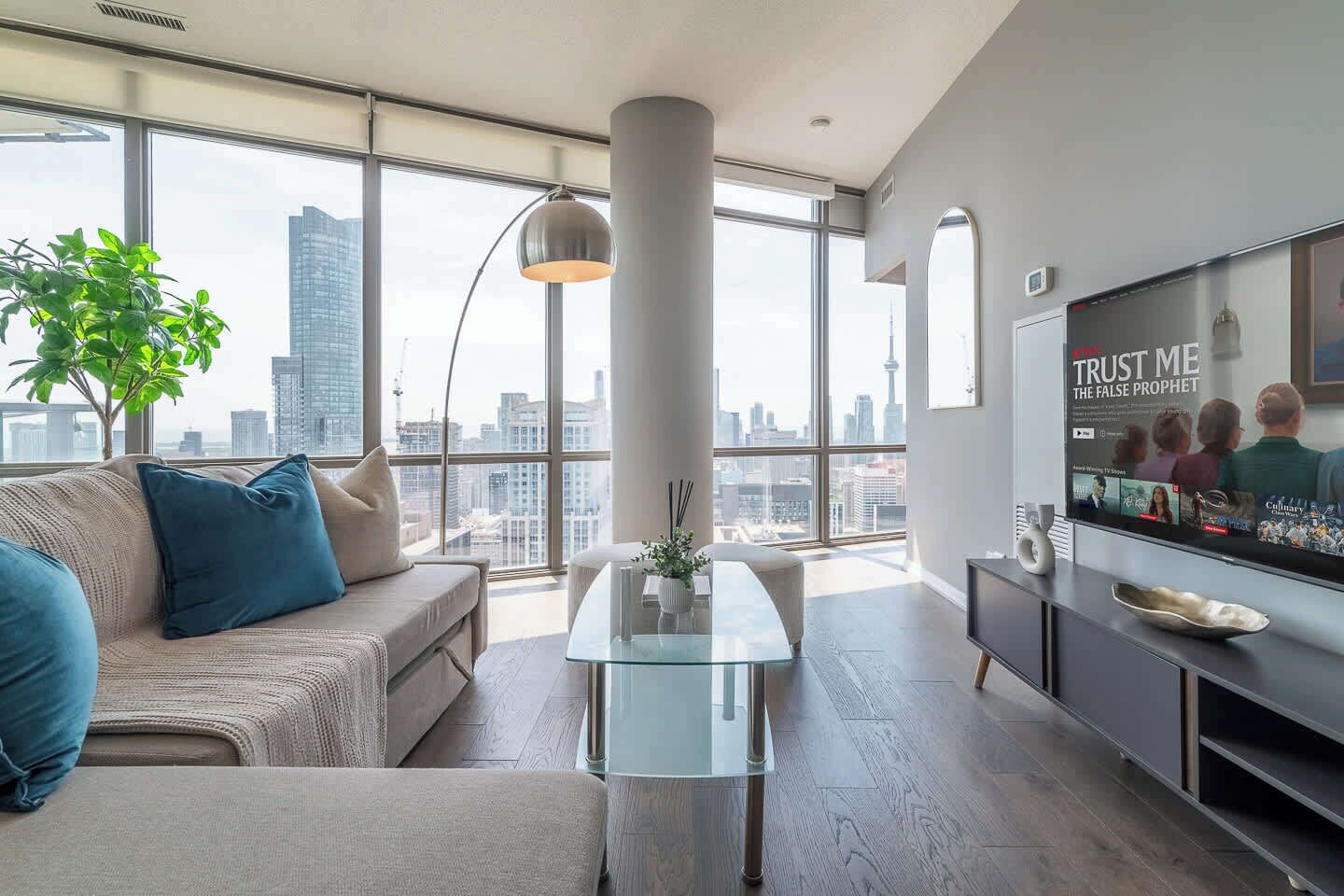 A modern living room with a sofa, a glass coffee table, and a TV mounted on the wall.