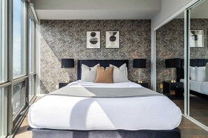 A modern bedroom with a large bed, two bedside lamps, and a city view.