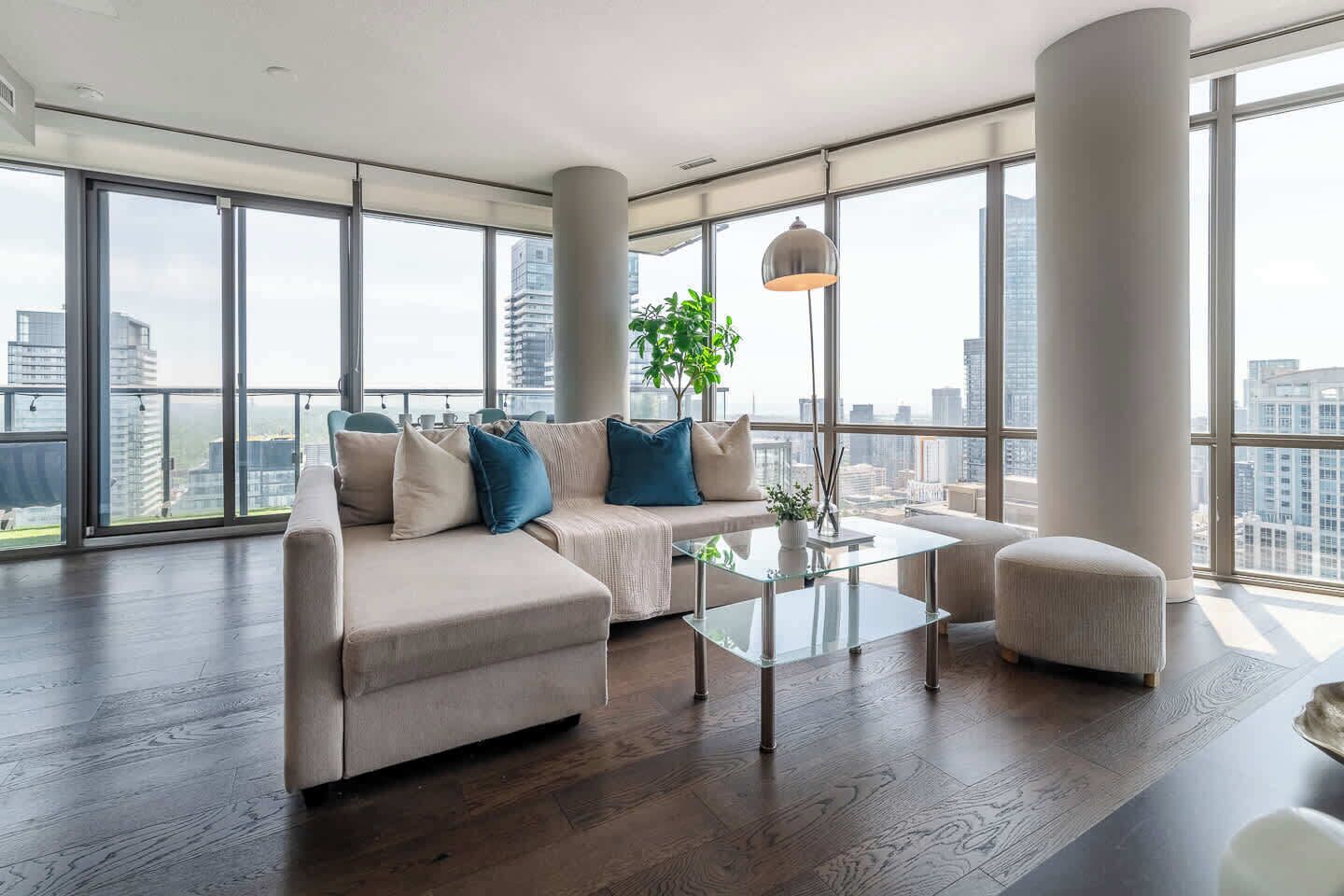 A modern living room with a sectional sofa, a glass coffee table, and a view of the city through large windows.